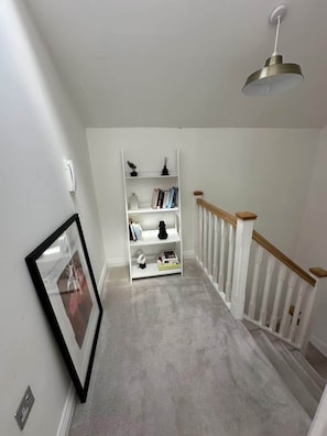 A hallway with a white staircase, a white bookshelf, and a hanging light fixture.