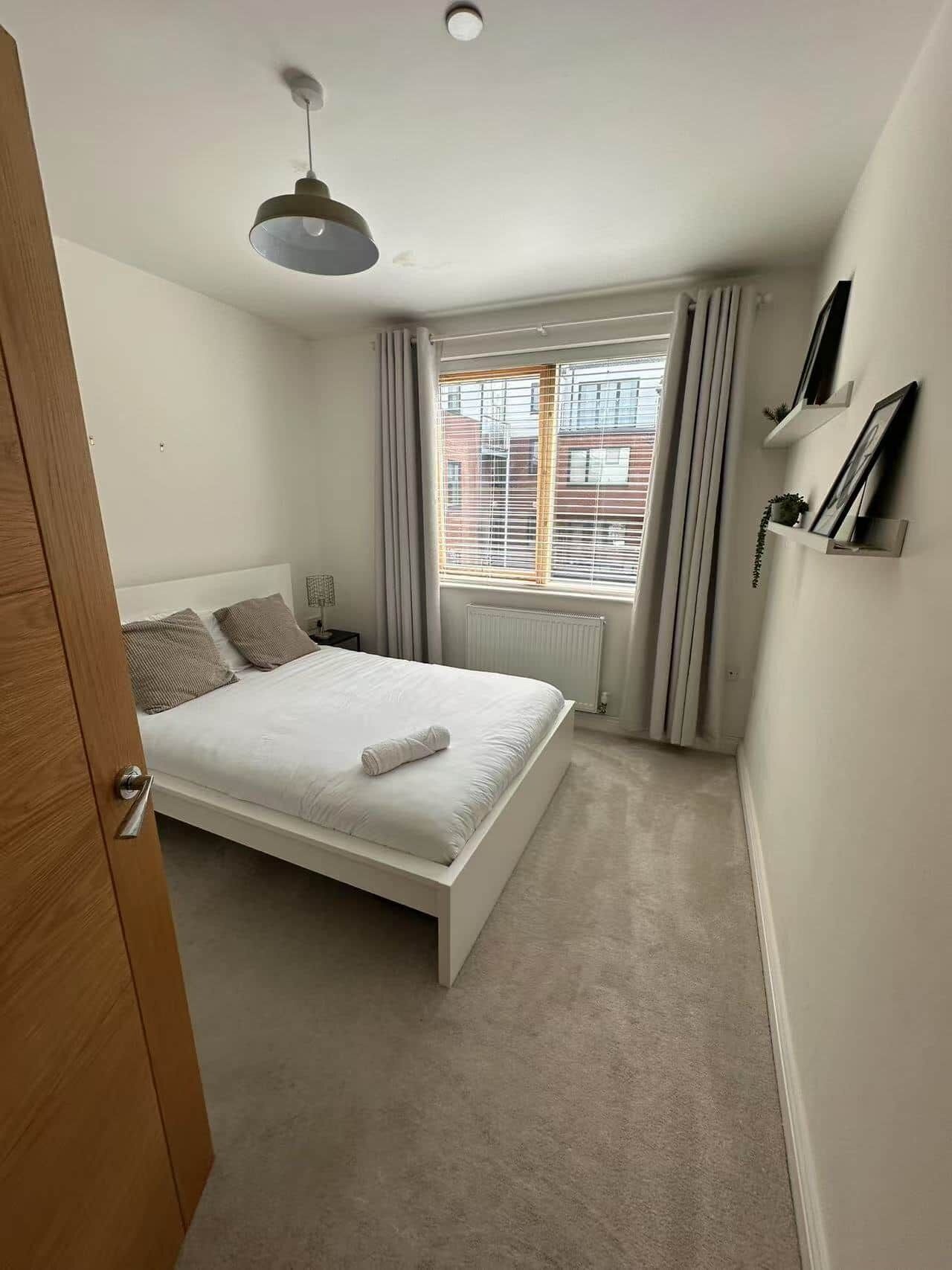 Une chambre à coucher avec un lit, un radiateur, une fenêtre avec des rideaux et un luminaire au plafond.