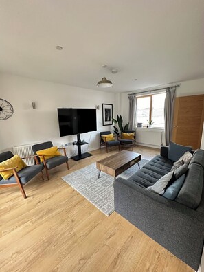 A modern living room with a flat-screen TV, a sofa, armchairs, and a coffee table.