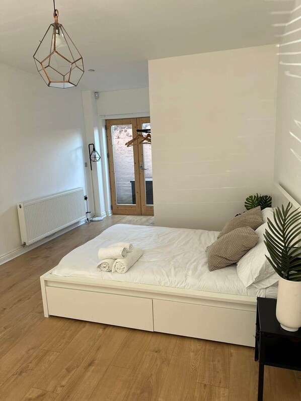 A bedroom with a bed, a radiator, a hanging light fixture, and a door leading to an outdoor area.