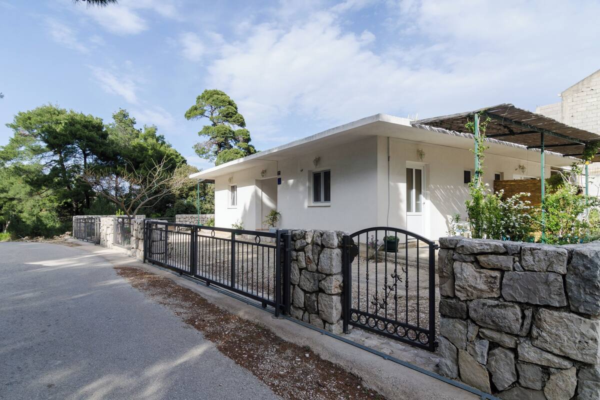 A single-story house with a stone wall and black metal fence.