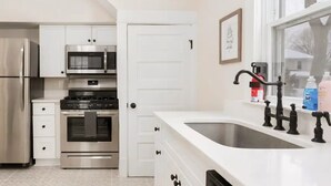 Una cocina moderna con electrodomésticos de acero inoxidable, una encimera blanca y un ventanal con vistas al exterior.