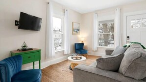 Una sala de estar moderna con un televisor de pantalla plana montado en la pared, una mesita auxiliar verde, un sillón azul, un sofá gris y una mesa de centro redonda.
