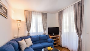 Ein Wohnzimmer mit einem blauen Sofa, einem Glastisch mit Obst und einem Fernseher auf einem Holzboden.