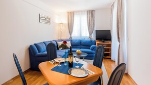 Ein Essbereich mit einem Tisch für zwei Personen, einem blauen Sofa, einem Fernseher und einem Fenster mit Vorhängen.