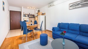 Ein modernes Wohnzimmer mit einem blauen Sofa, einer Essecke mit Tisch und Stühlen sowie einer Küche im Hintergrund.
