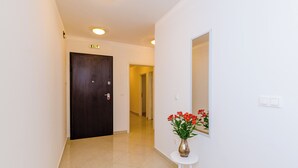 A hallway with a dark wooden door, a white wall, and a small table with a vase of flowers. - Grand Apartment (Dubrovnik)