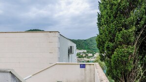A building with a sign indicating "21A" and a view of a hillside with trees and a body of water in the background. - Grand Apartment (Dubrovnik)