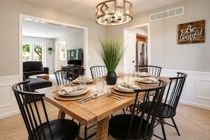 A dining room with a wooden table set for six, surrounded by black chairs, a potted plant, and a chandelier. - Spacious 6-Bed Luxury Home Near Notre Dame (Granger)