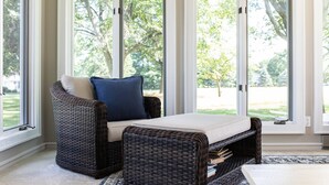 Un sofá de mimbre con un cojín y una pequeña mesa en una habitación con ventanas amplias.