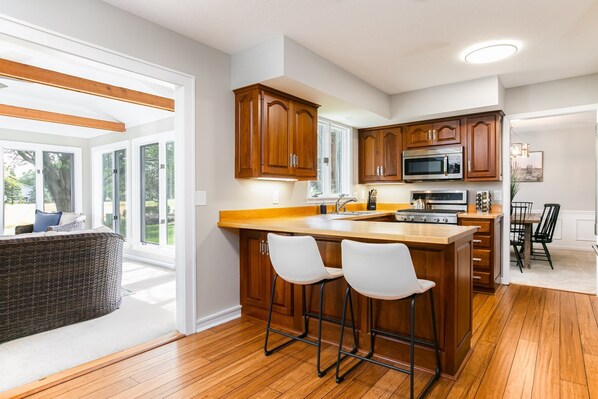 A modern kitchen with wooden cabinets, a large island with bar stools, a microwave, and a stove. - Spacious 6-Bed Luxury Home Near Notre Dame (Granger)