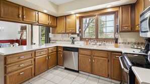 Una cocina moderna con armarios de madera, lavavajillas, estufa y un amplio ventanal que proporciona luz natural.
