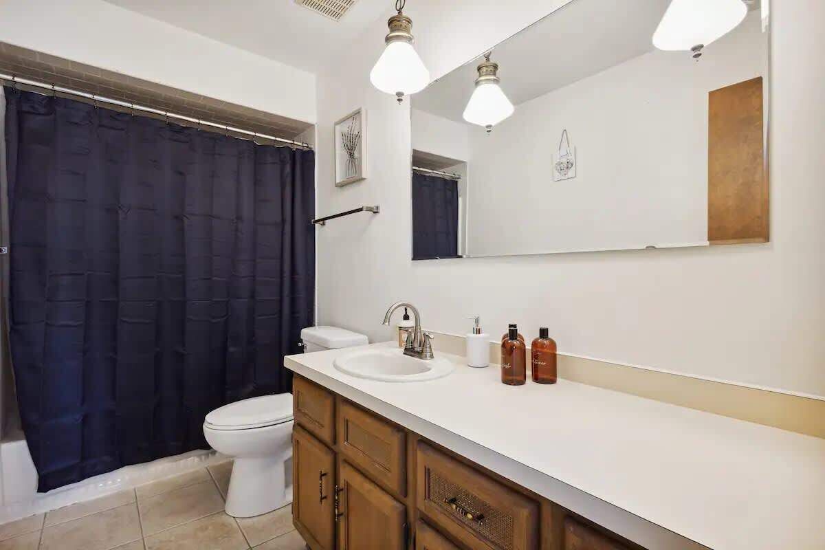 A bathroom with a white sink, wooden cabinets, a toilet, and a dark shower curtain.