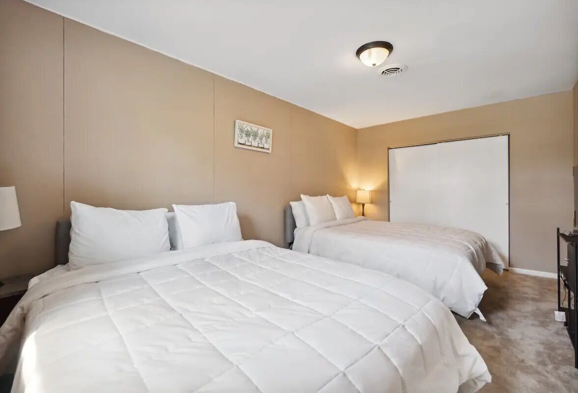 A hotel room with two beds, beige walls, a ceiling light, and a whiteboard.