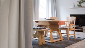 Un comedor con una mesa y sillas de madera, un televisor y una estantería con objetos decorativos.