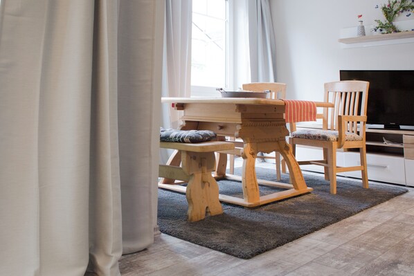 A dining area with a wooden table and chairs, a television, and a shelf with decorative items.