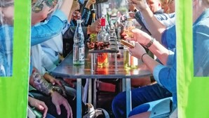 Un grupo de personas brindando con bebidas alrededor de una mesa dentro de una estructura con techo verde.