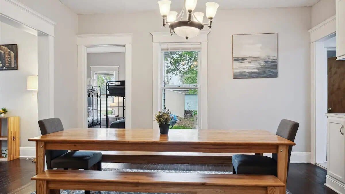 Een eetkamer met een houten tafel, bankjes en een kroonluchter.