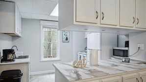 Una cocina moderna con gabinetes blancos, encimera de mármol y un cubo de basura.