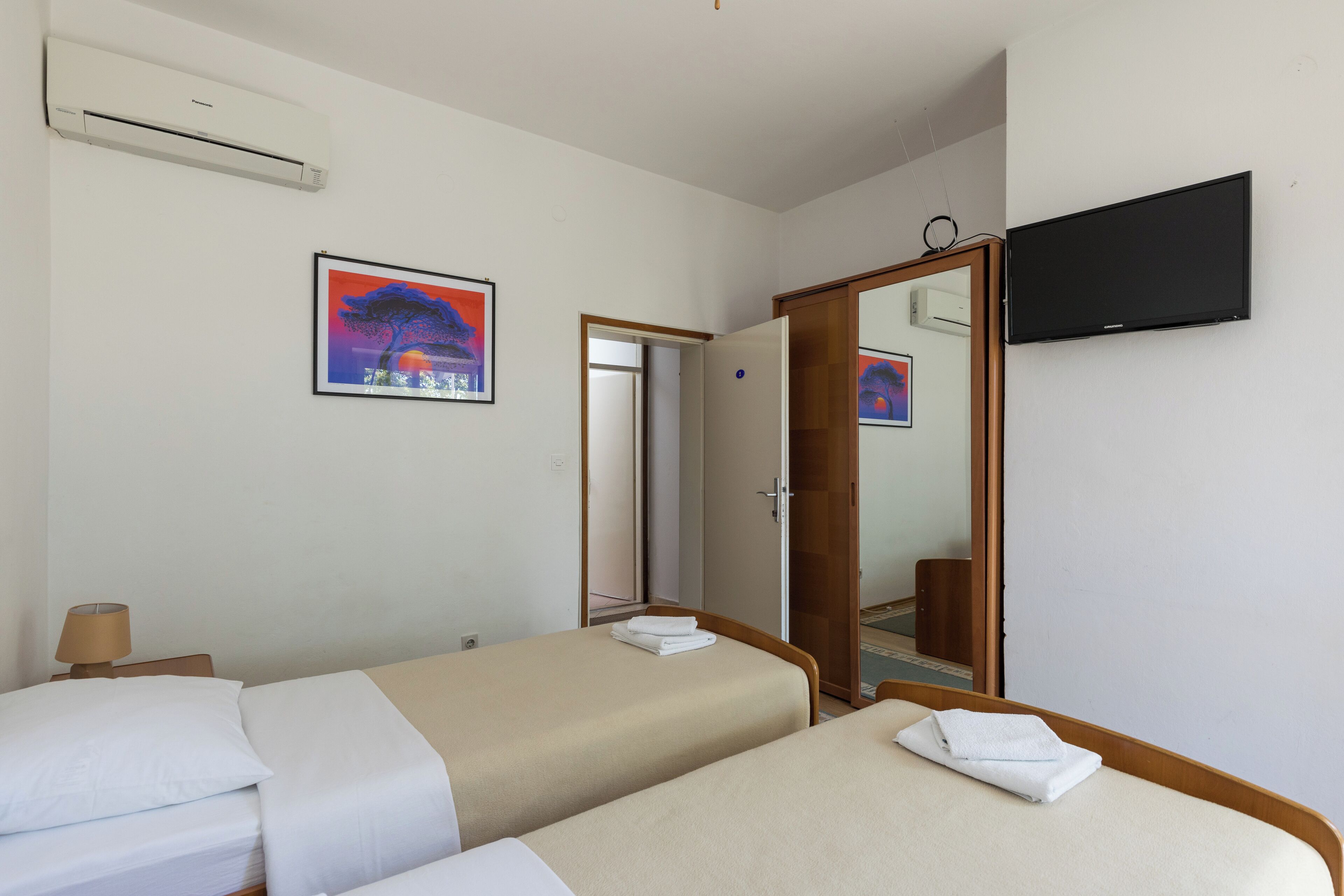 Habitación de hotel con dos camas, una televisión de pantalla plana, un cuadro y un equipo de aire acondicionado.