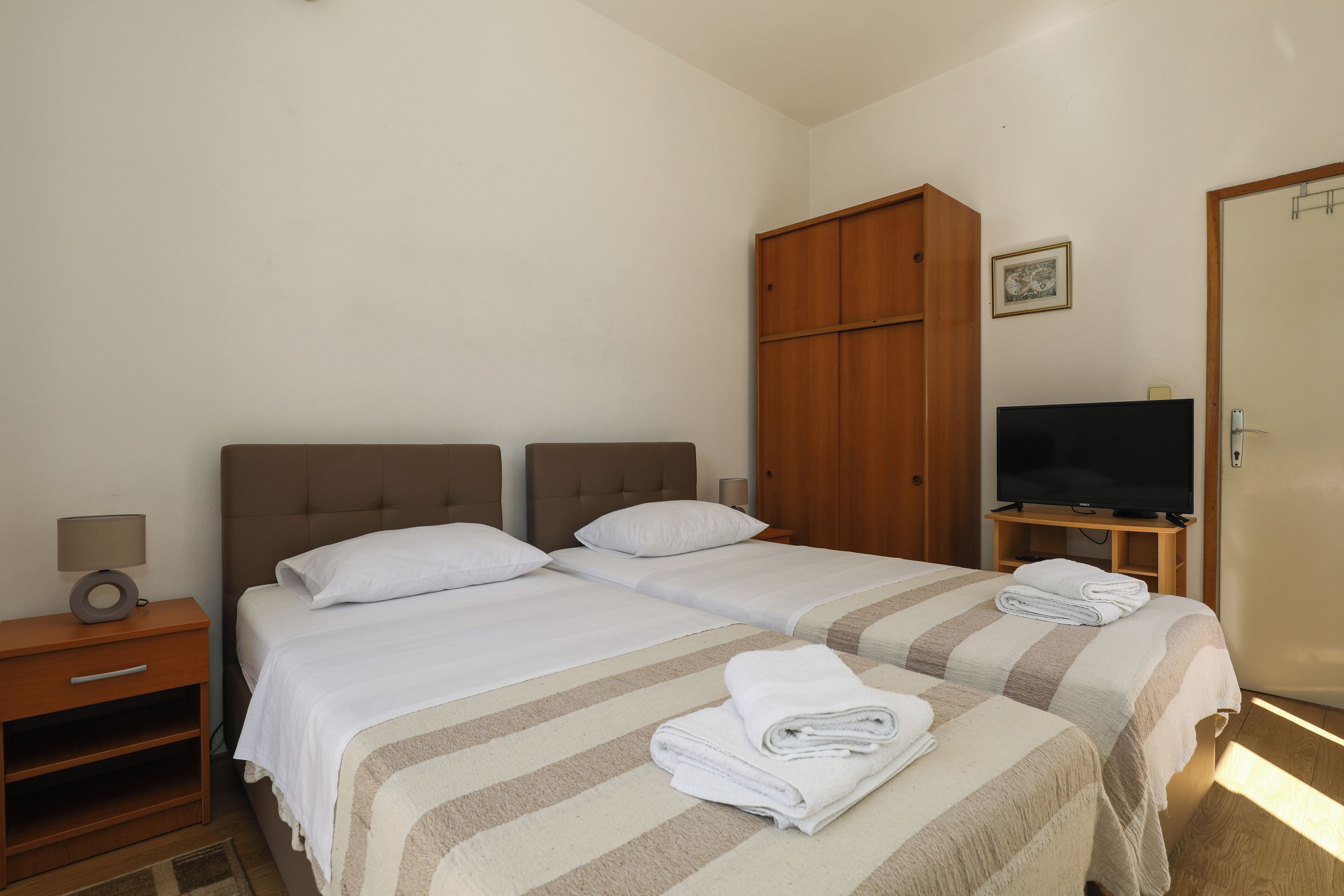 Une chambre d’hôtel avec deux lits, une armoire, une télévision et une table de chevet avec une lampe.