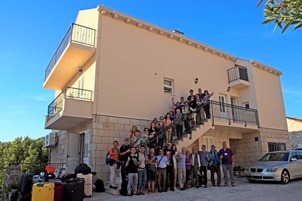 A group of people standing on a staircase outside a building with a beige facade and balconies.