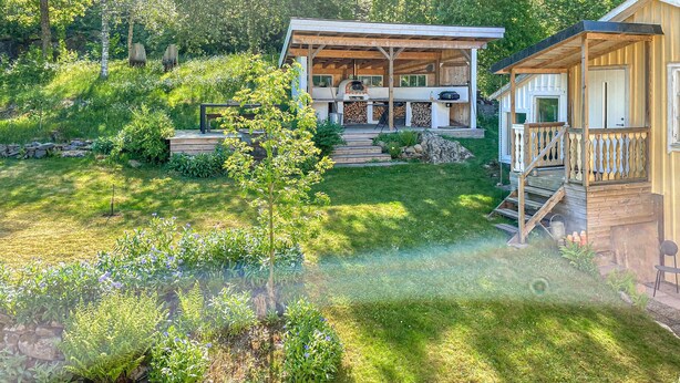 Une cabane rustique dotée d’un porche couvert, d’un mur en pierre et d’une petite terrasse.