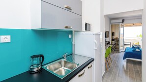 Cuina moderna amb un rentaplat, una vitroceràmica i un refrigerador petit. Es veu una zona de menjador amb taula i cadires a través d'una porta oberta.
