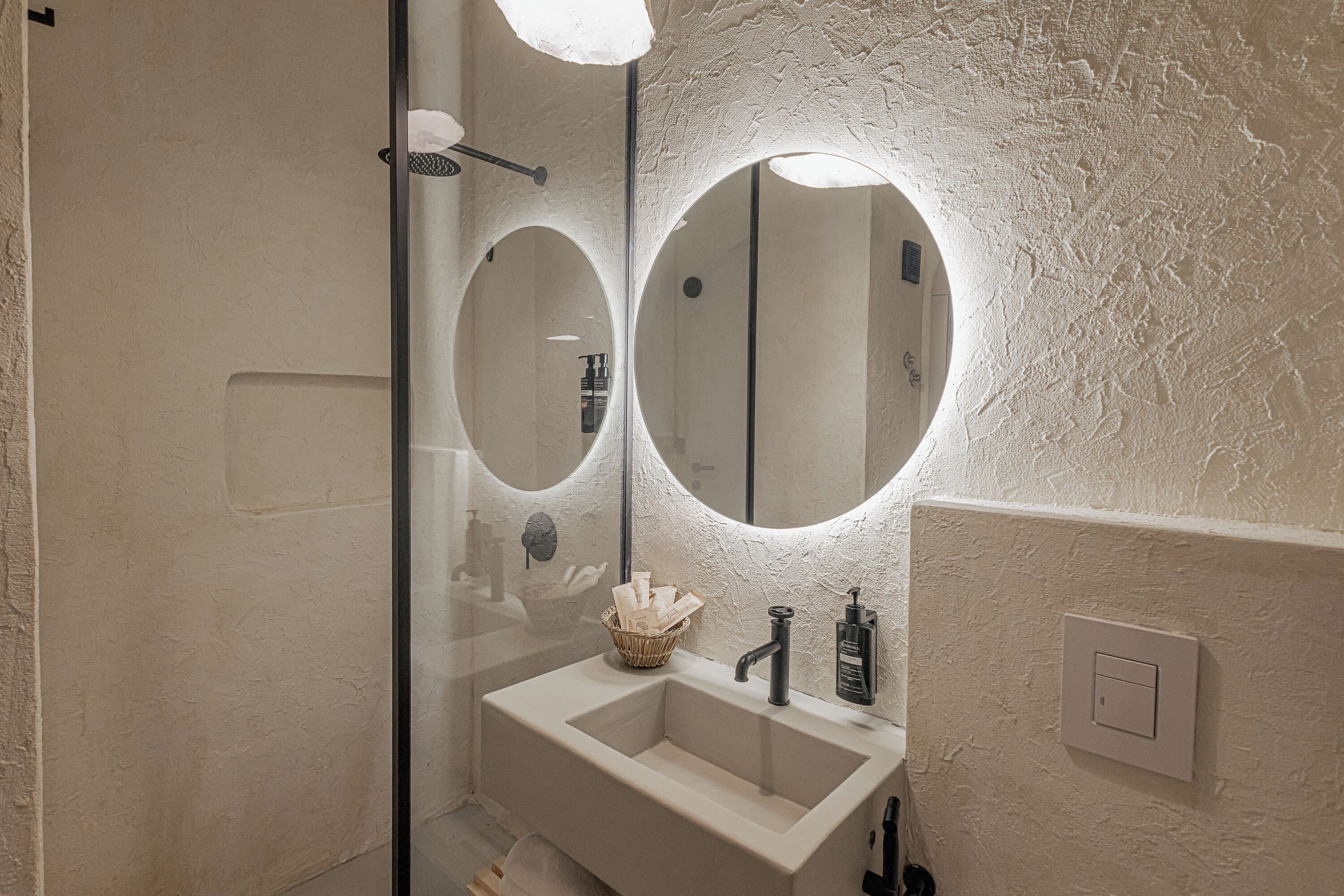 A bathroom with a white sink, two round mirrors, and a textured wall.