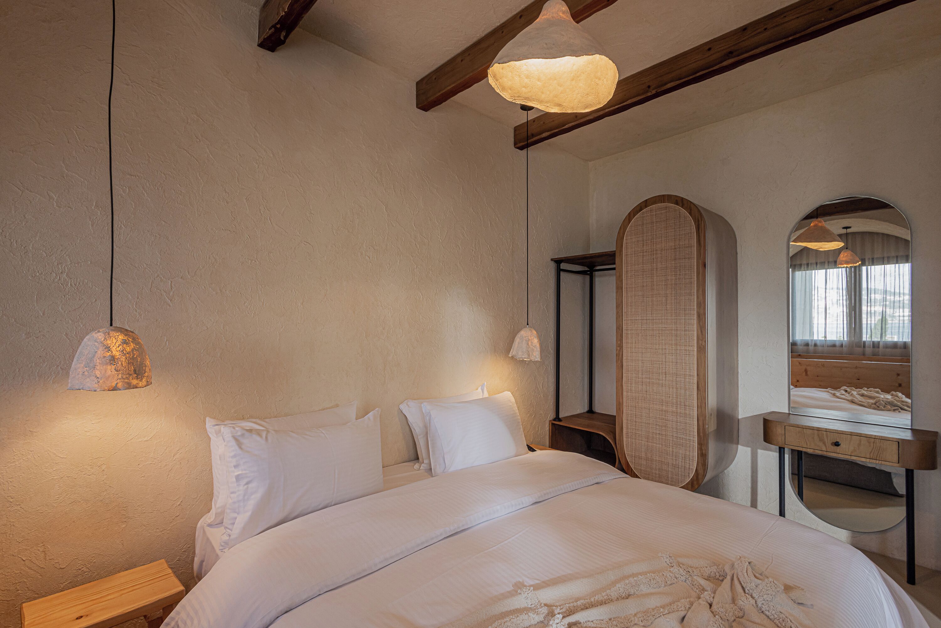 Un dormitorio con una cama grande, cabecera de madera, mesitas de noche, un espejo y una lámpara colgante.