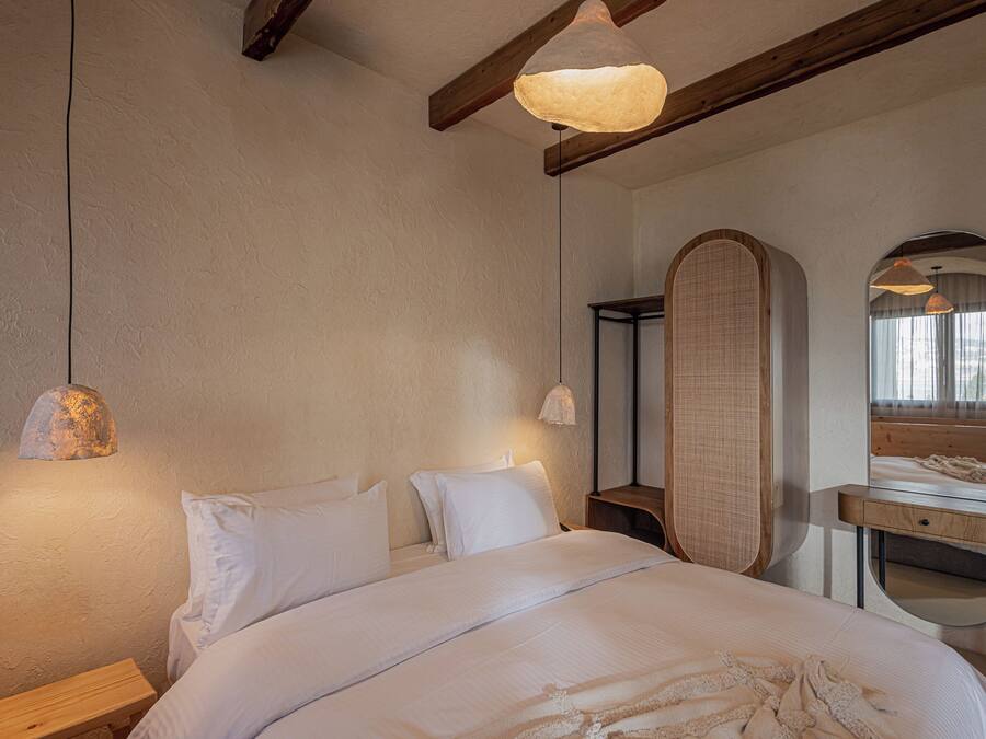Un dormitorio con una cama grande, cabecera de madera, mesitas de noche, un espejo y una lámpara colgante.