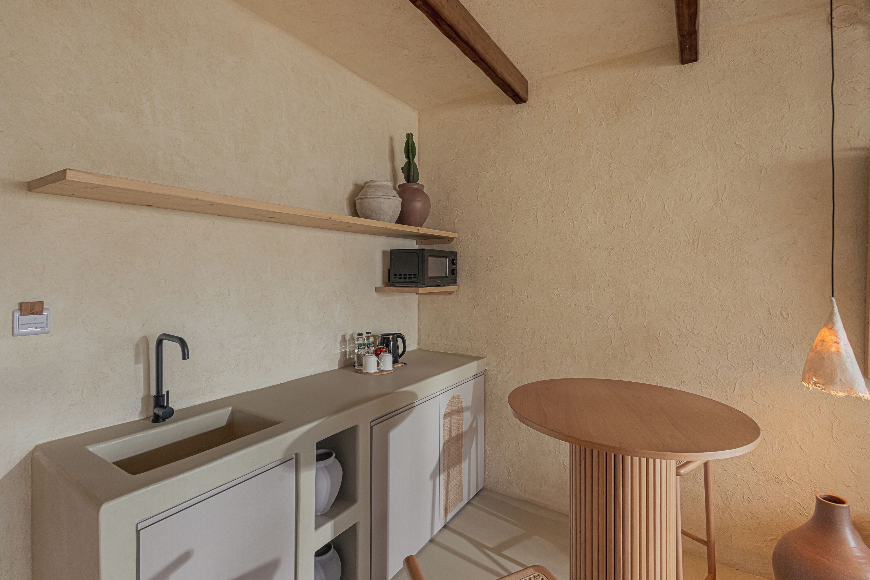 A modern kitchen with a built-in sink, wooden shelves, a microwave, and a round wooden table.