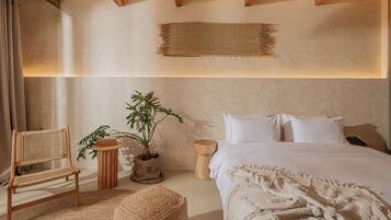 A bedroom with a bed, a chair, a small table, and a potted plant.