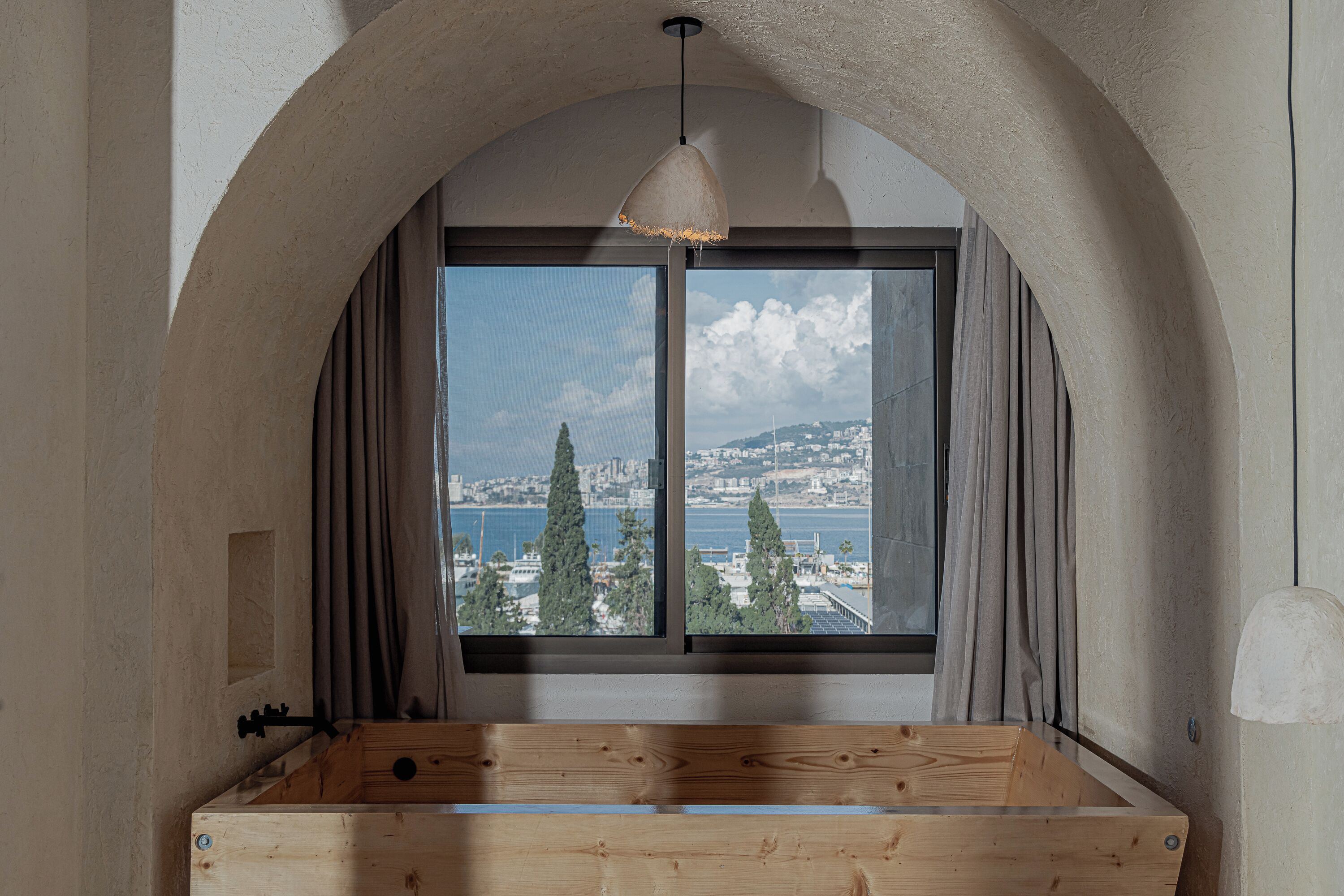 Una habitación con un amplio ventanal de arco, un banco de madera y vistas a la ciudad y al agua.