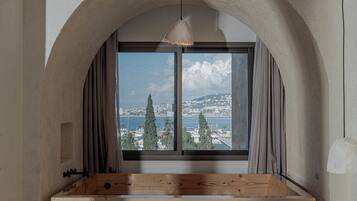 Una habitación con un amplio ventanal de arco, un banco de madera y vistas a la ciudad y al agua.
