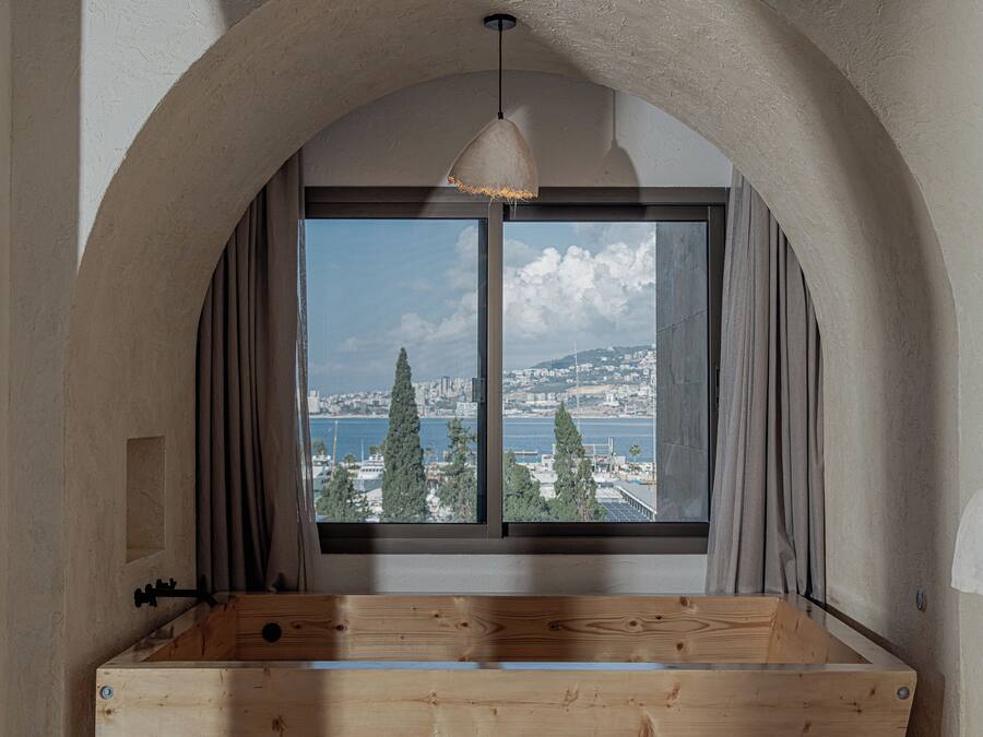 A room with a large arched window, a wooden bench, and a view of a cityscape and water.