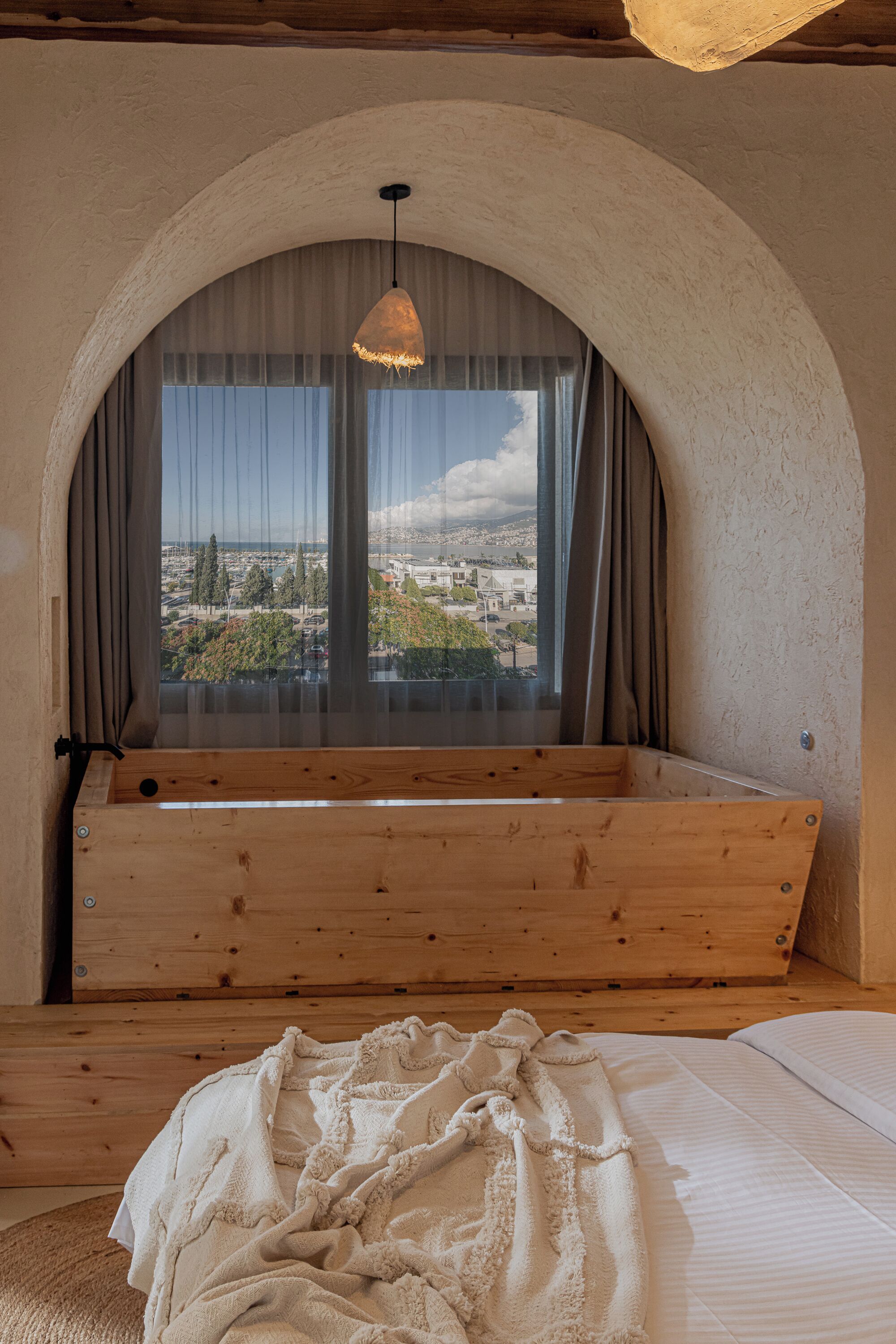 A cozy room with a wooden bench, a large window with curtains, and a hanging light fixture.