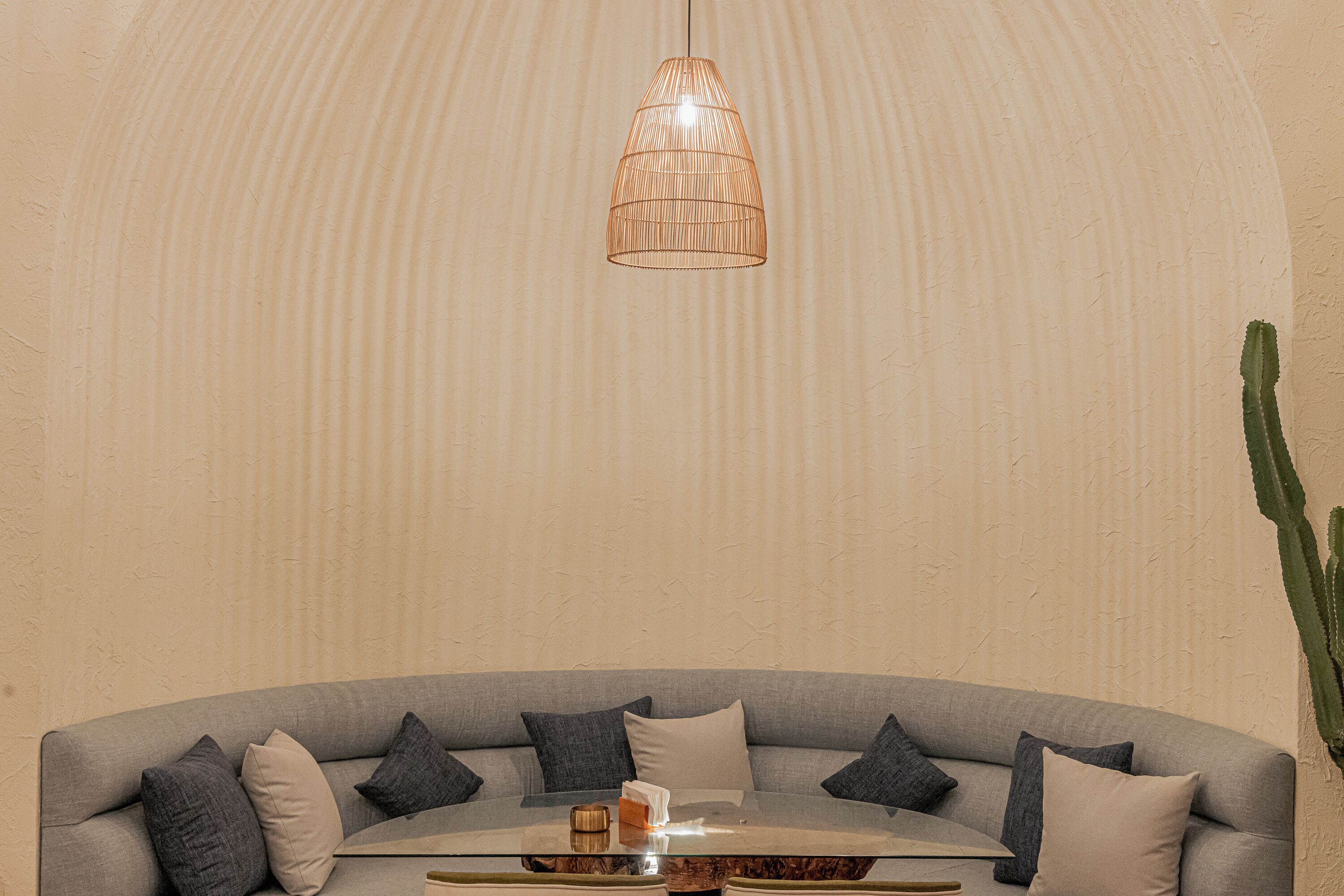 Una sala de estar moderna con un sofá gris curvo, una mesa de centro redonda de vidrio y una lámpara colgante.