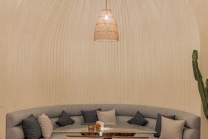 Una sala de estar moderna con un sofá gris curvo, una mesa de centro redonda de vidrio y una lámpara colgante.