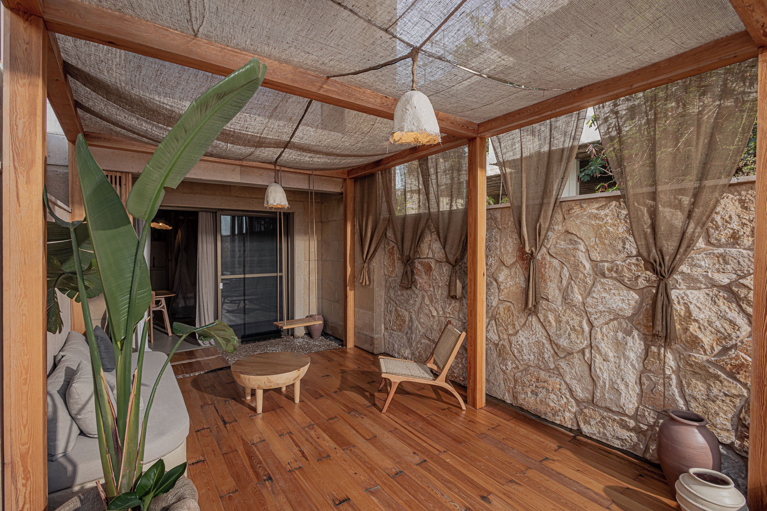 A room with wooden flooring, a stone wall, a wooden ceiling, and a large window with curtains.