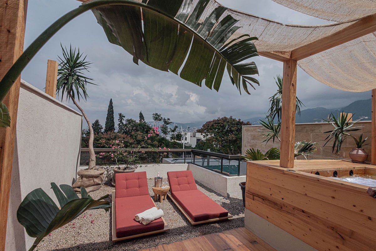 A rooftop terrace with two red lounge chairs, a small table, and a wooden deck.