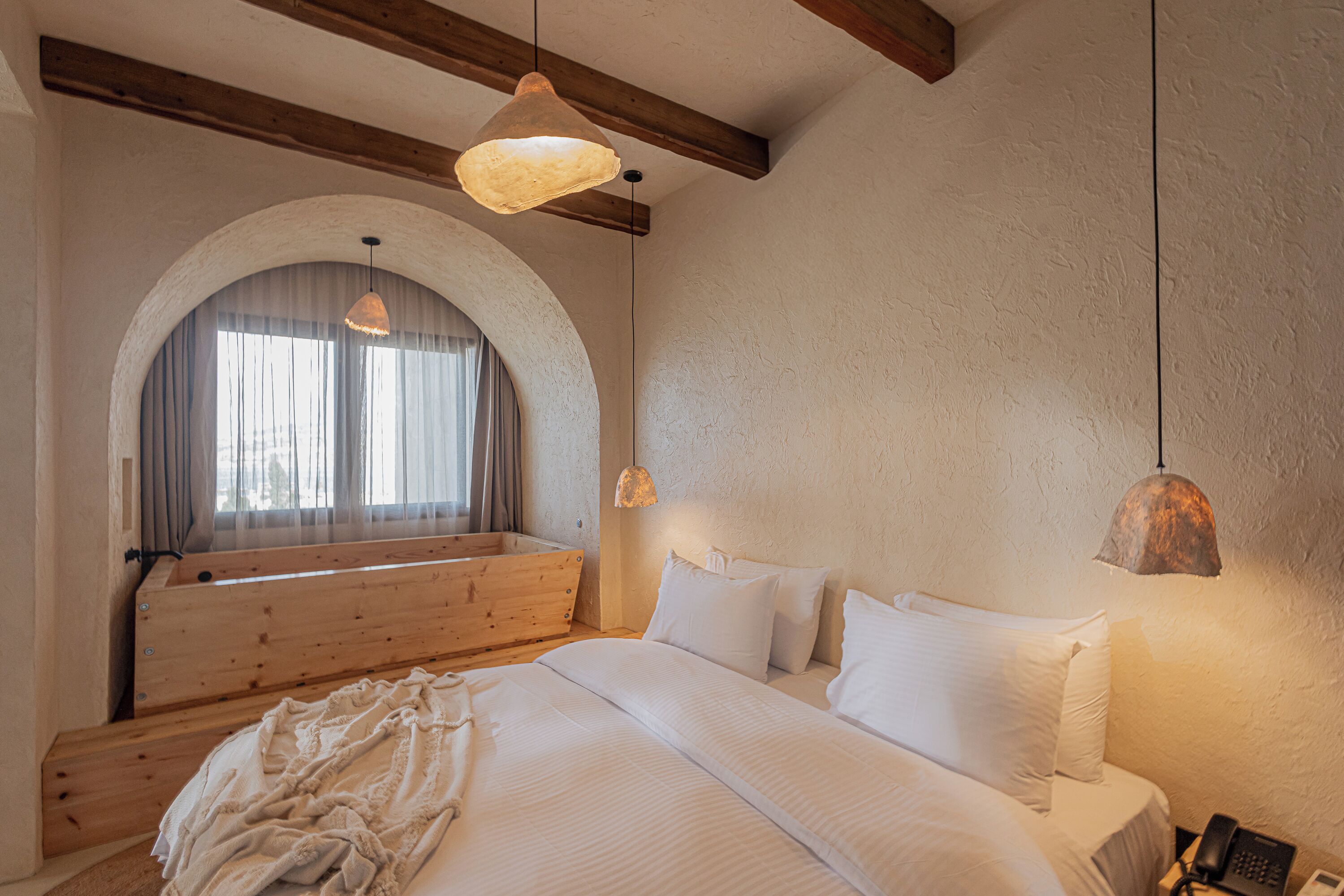 A bedroom with a large bed, wooden headboard, arched window, and two pendant lights.