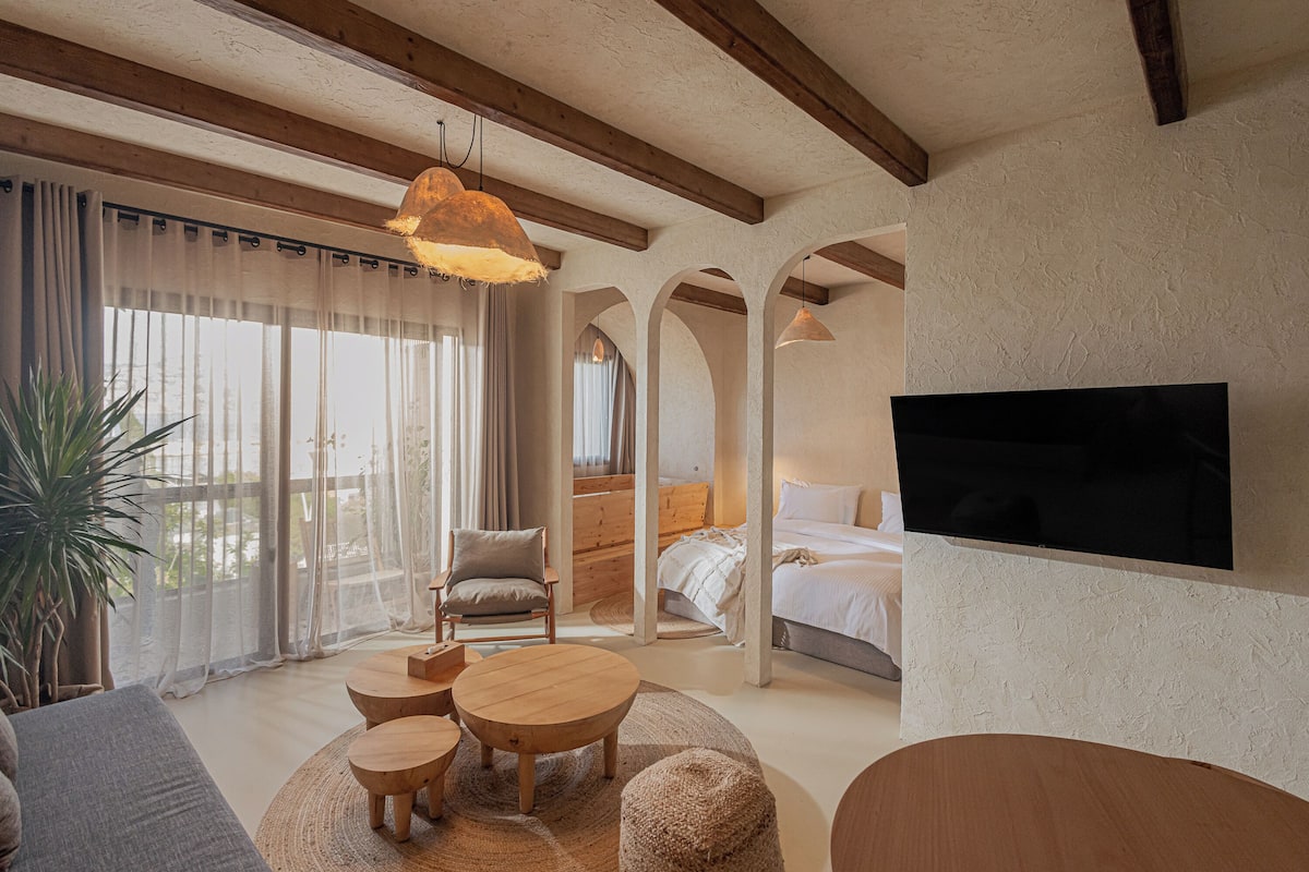 A modern bedroom with a large bed, a TV mounted on the wall, and a cozy seating area with a round table and chairs.