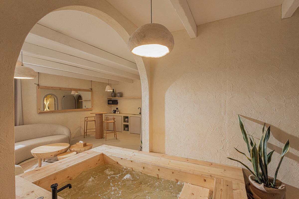 A spa area with a wooden bathtub, a sink, and a mirror. There is a plant and a hanging light fixture.
