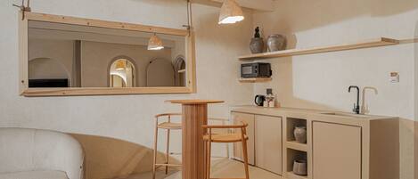 Una cocina minimalista con una mesa de madera, dos taburetes altos y electrodomésticos como un microondas y una cafetera.