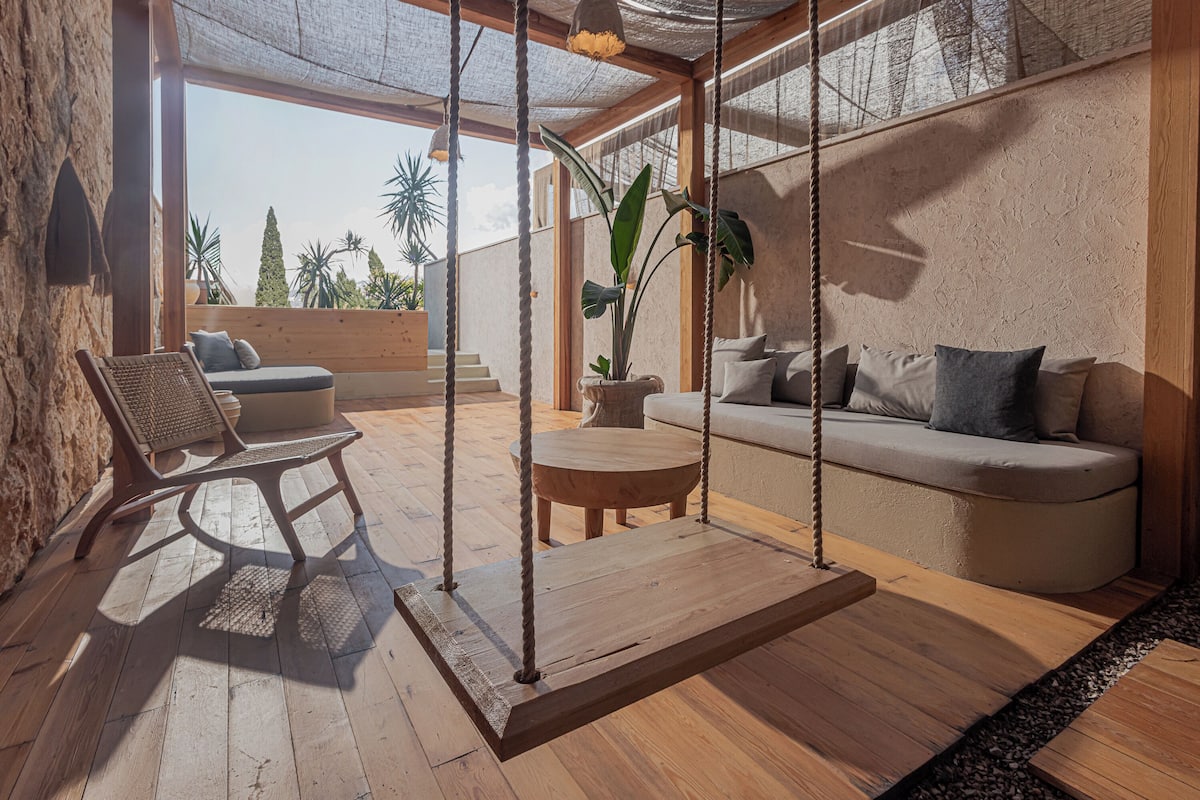 A modern interior with a wooden floor, a swing chair, a sofa, and a potted plant.