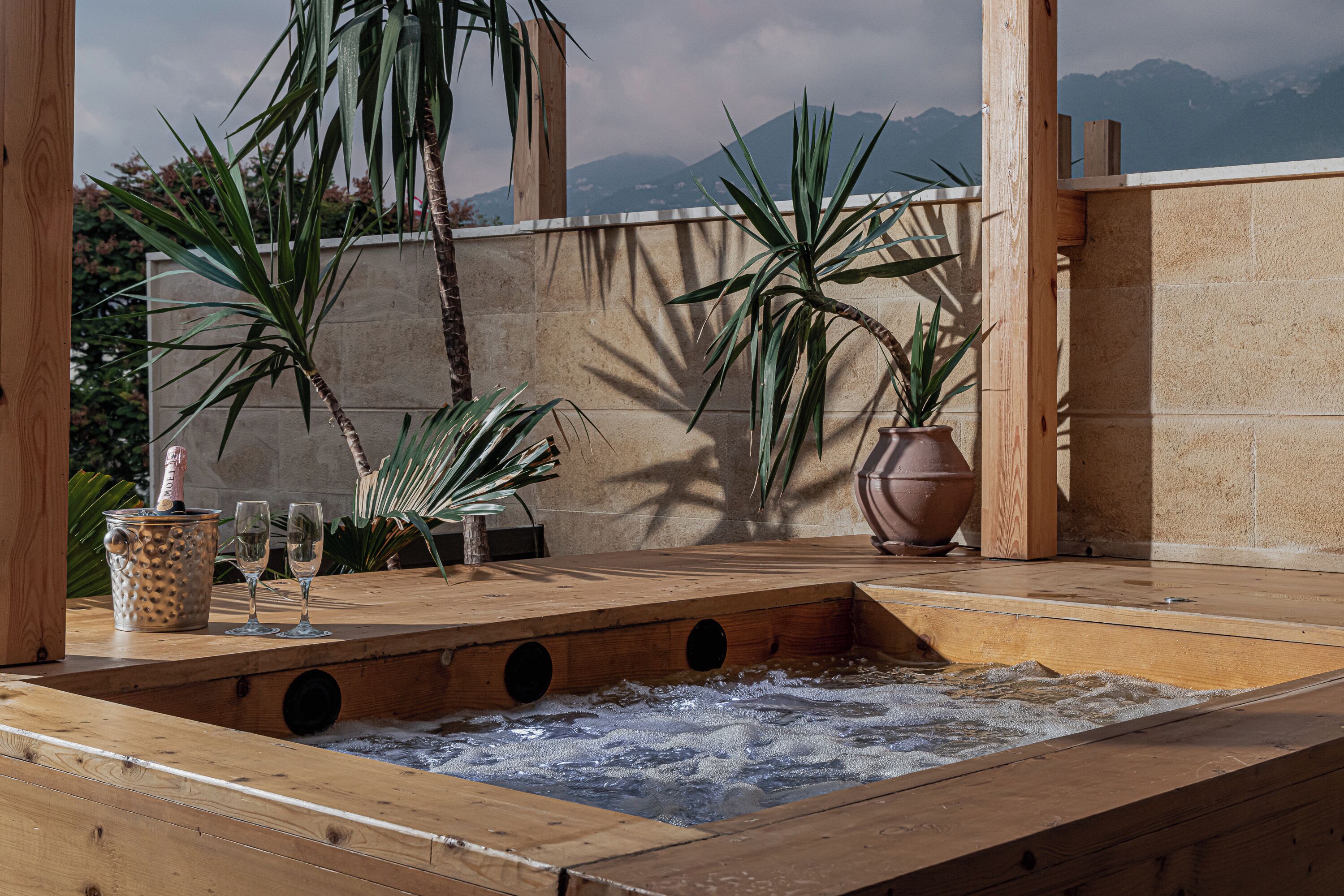 Ein Whirlpool mit Holzterrasse, umgeben von Blumentöpfen und einer Steinmauer, mit Blick auf eine Berglandschaft.