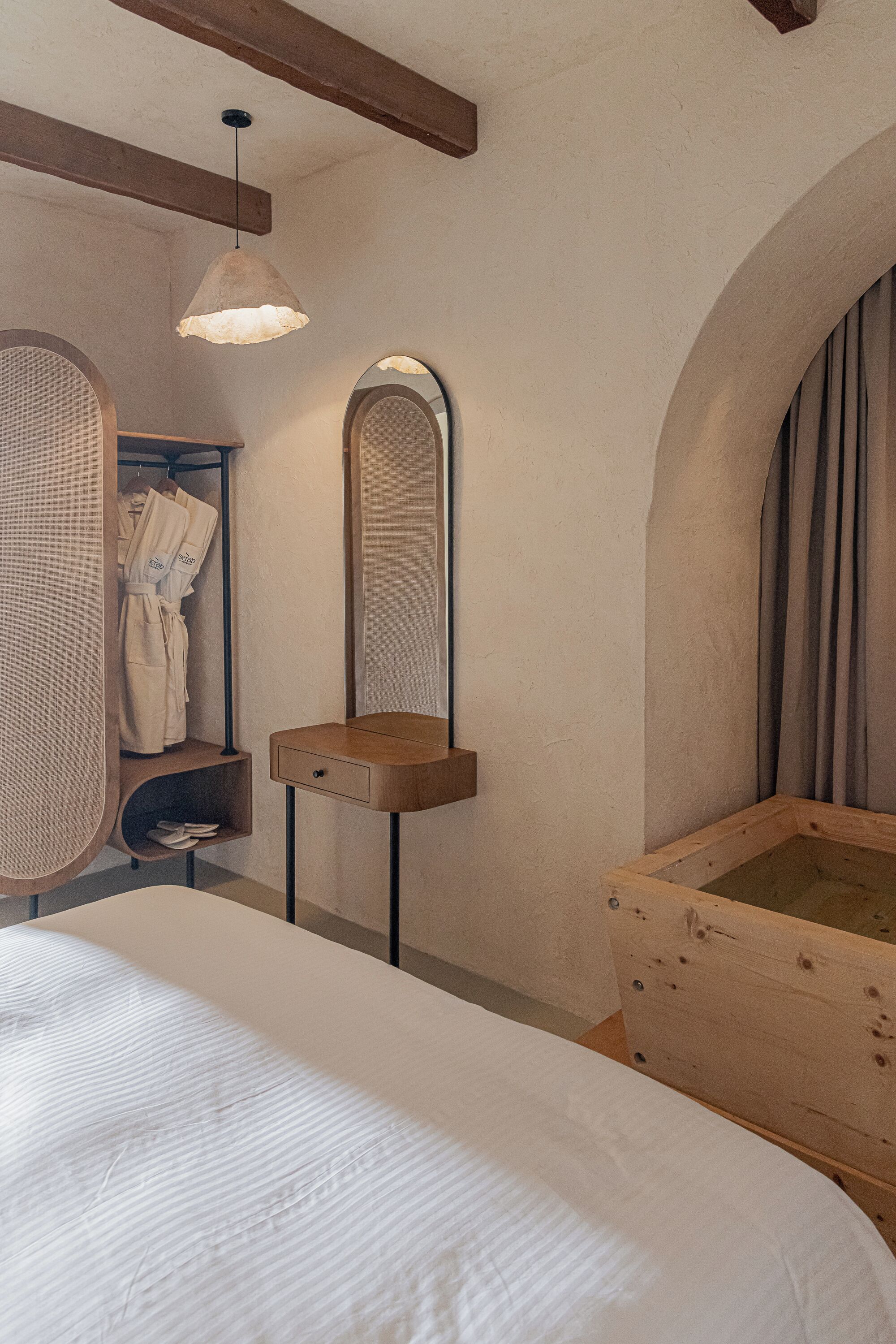 Ein Schlafzimmer mit einem großen Bett, einem Nachttisch aus Holz, einer Pendelleuchte, einer Holzbadewanne und einem Spiegel an der Wand.