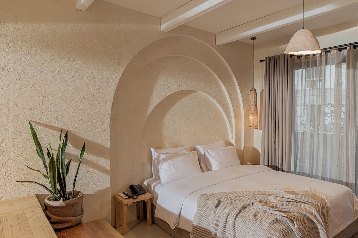 A bedroom with a bed, bedside table, lamp, and a potted plant.