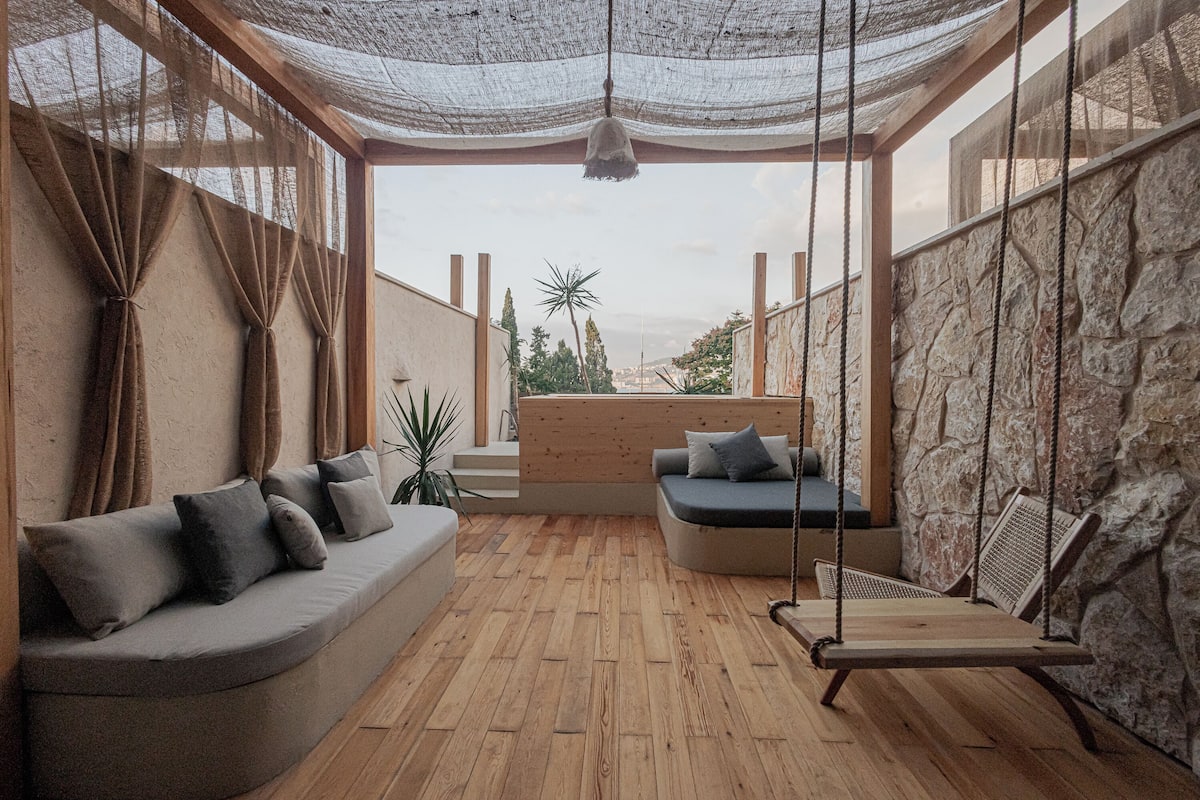 A cozy outdoor seating area with a wooden floor, cushioned seating, and a swing.